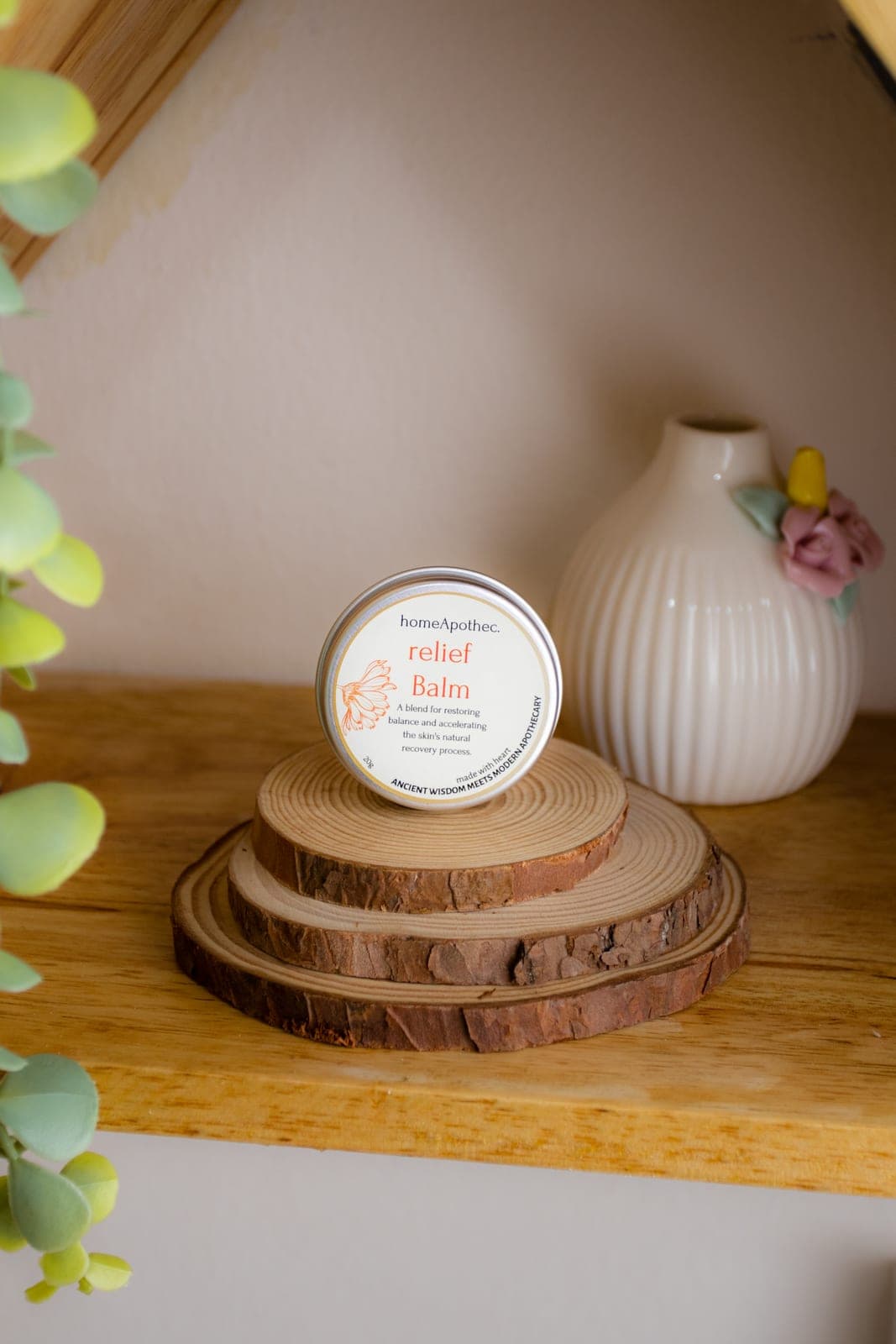 A Relief Balm tin on stacked wood slices on a home shelf beside a white vase