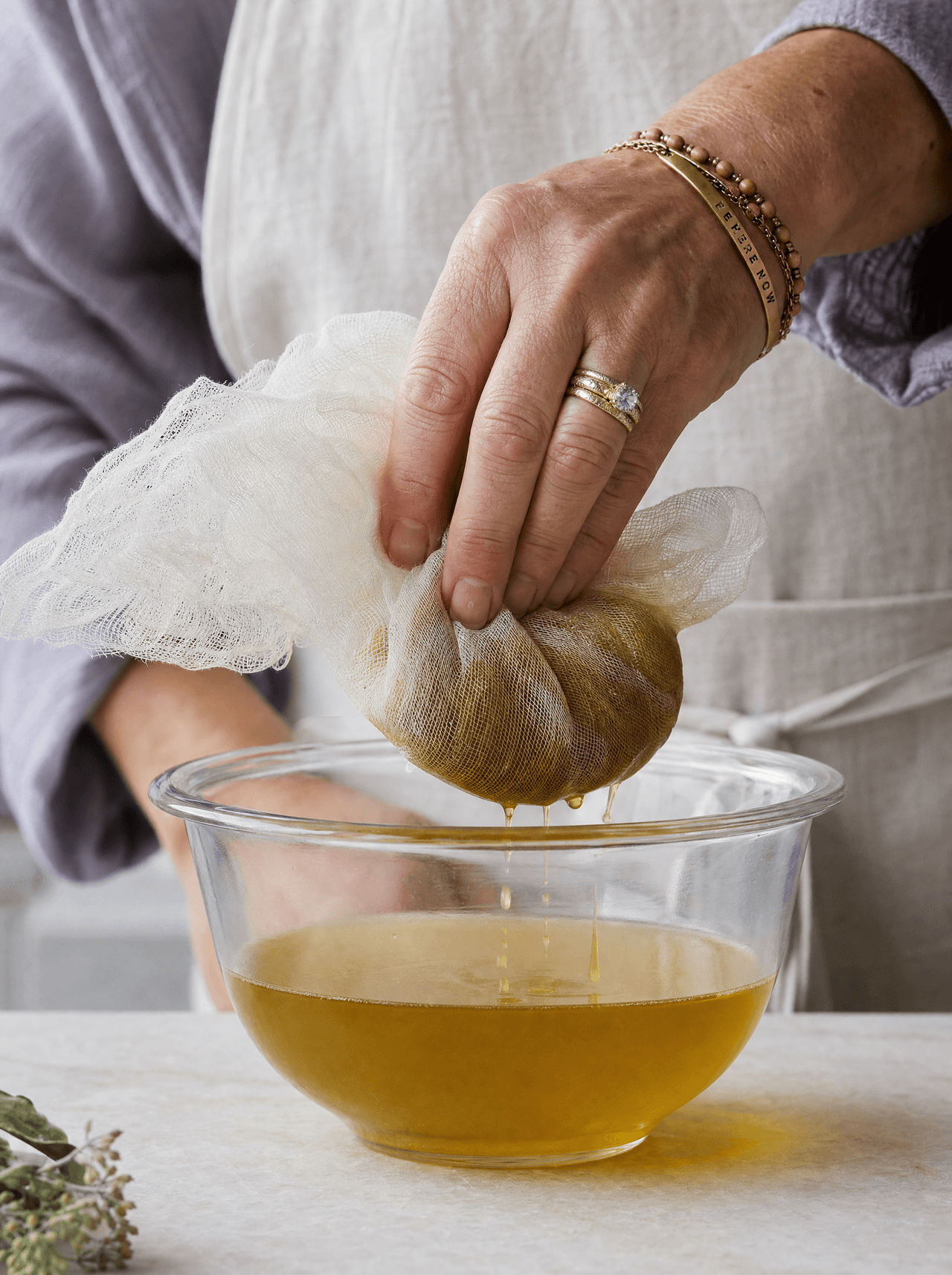 Straining botanical oil through fine cloth — the final step after 8 weeks